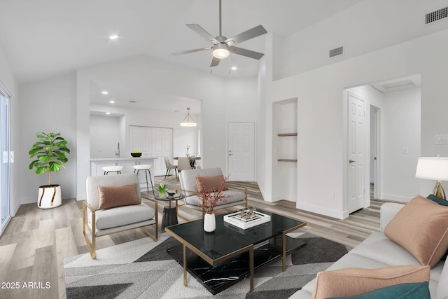 living room with ceiling fan, built in features, high vaulted ceiling, and light hardwood / wood-style flooring