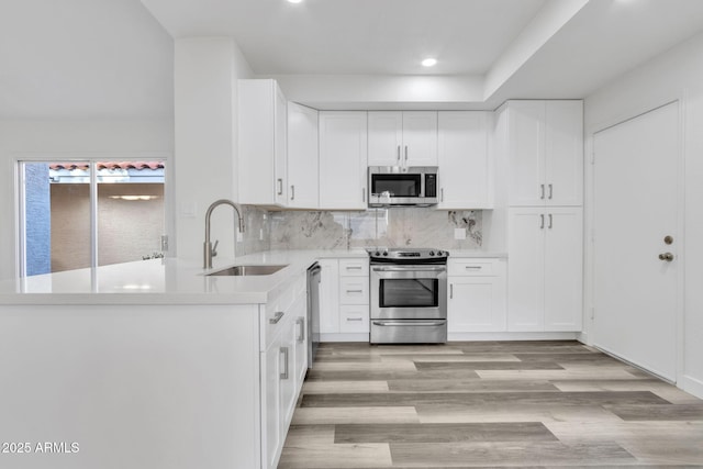 kitchen featuring sink, appliances with stainless steel finishes, light hardwood / wood-style floors, decorative backsplash, and white cabinets