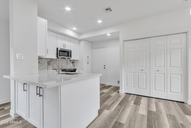 kitchen featuring white cabinetry, sink, light hardwood / wood-style flooring, and kitchen peninsula