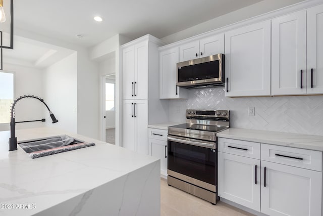 kitchen featuring white cabinetry, sink, appliances with stainless steel finishes, tasteful backsplash, and light stone countertops