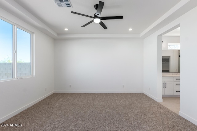 carpeted empty room with ceiling fan and a raised ceiling