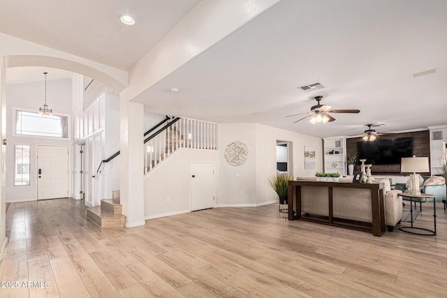 living room featuring built in shelves, ceiling fan with notable chandelier, and light hardwood / wood-style floors