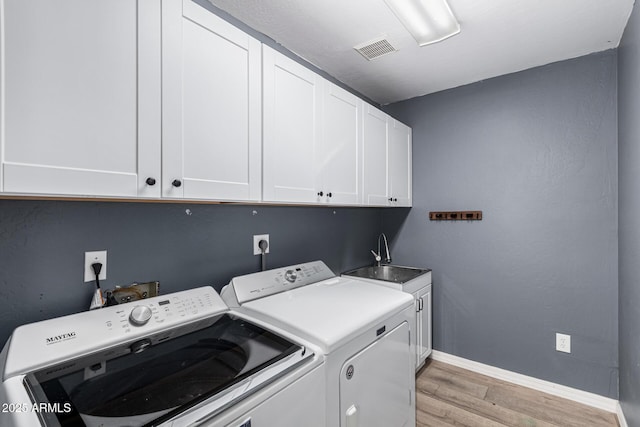 laundry area with light wood-type flooring, cabinets, sink, and washing machine and clothes dryer