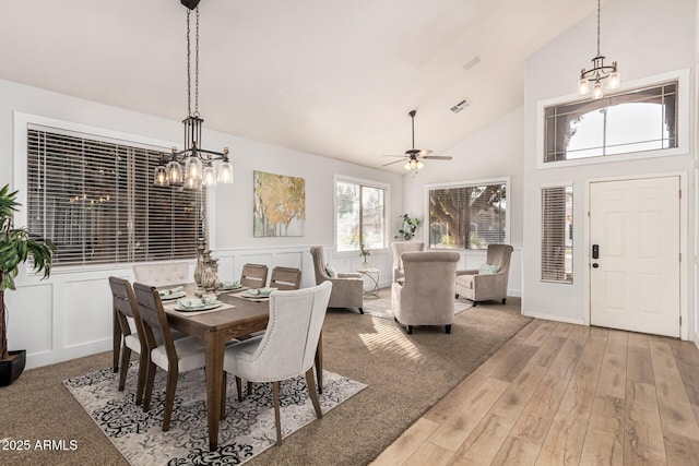 dining area with ceiling fan with notable chandelier, high vaulted ceiling, and light hardwood / wood-style floors