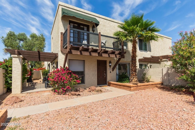 view of front facade featuring fence, a balcony, a patio, a pergola, and stucco siding
