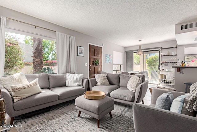 living room with visible vents, a textured ceiling, a notable chandelier, and a wealth of natural light
