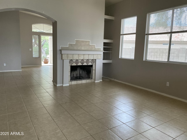 unfurnished living room with tile patterned flooring, built in shelves, a fireplace, and baseboards