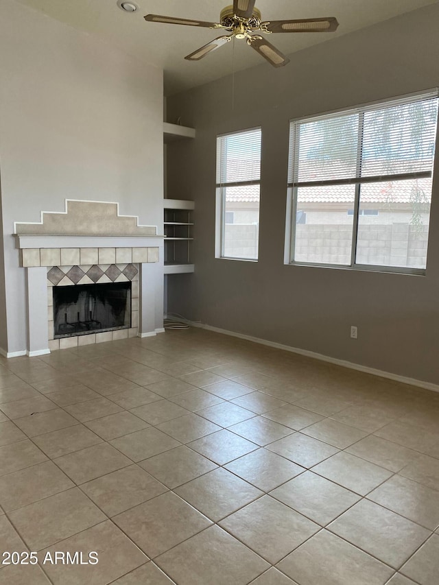 unfurnished living room with a tiled fireplace, built in features, baseboards, and light tile patterned flooring