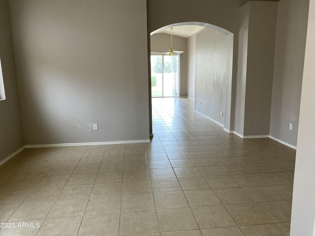 spare room featuring light tile patterned floors, baseboards, arched walkways, and ceiling fan