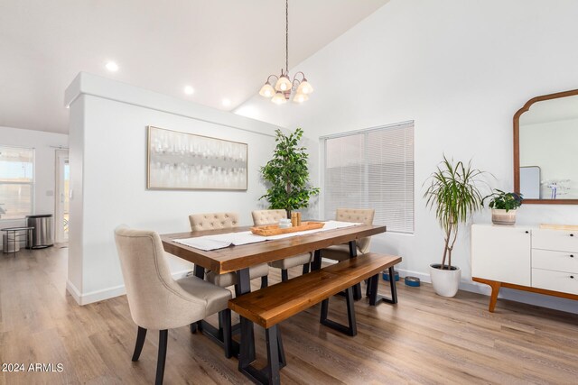 dining space with high vaulted ceiling, light hardwood / wood-style flooring, and an inviting chandelier