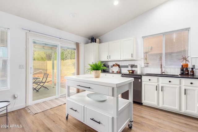 kitchen with stainless steel dishwasher, sink, vaulted ceiling, and white cabinetry