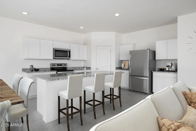 kitchen featuring a kitchen bar, a center island with sink, stainless steel appliances, white cabinets, and light stone counters