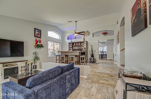 living room featuring ceiling fan, indoor bar, vaulted ceiling, and light hardwood / wood-style floors