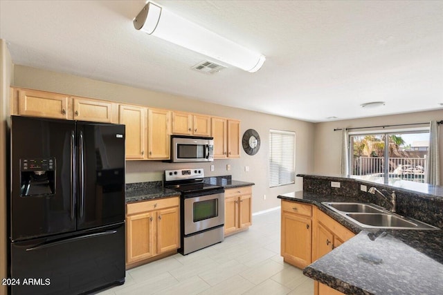 kitchen with appliances with stainless steel finishes, light brown cabinets, dark stone countertops, and sink