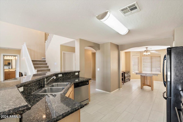 kitchen with dishwasher, black fridge, dark stone counters, sink, and a textured ceiling