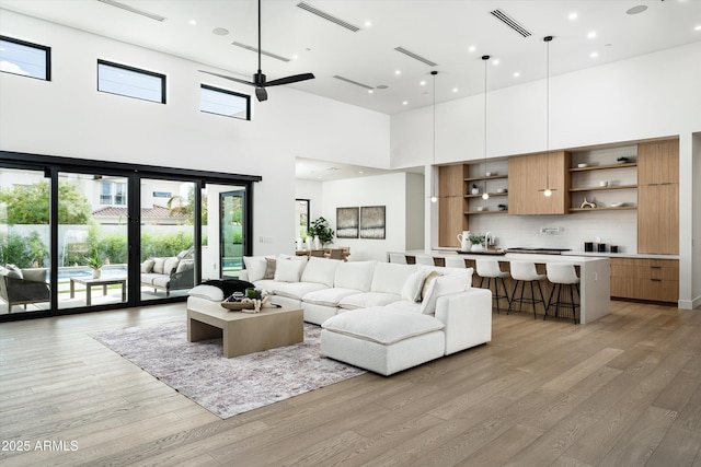 living room featuring light wood-type flooring, a towering ceiling, visible vents, and a ceiling fan