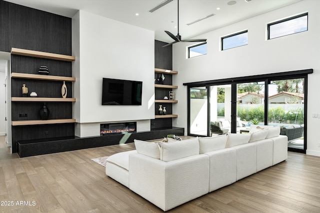 living room with a glass covered fireplace, visible vents, a towering ceiling, and wood finished floors