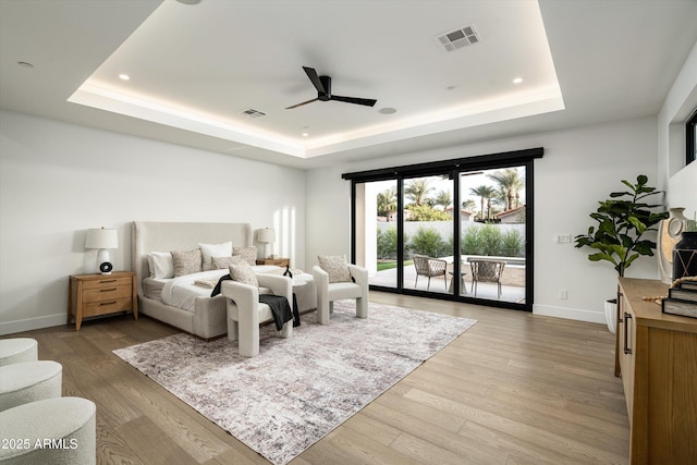 bedroom with access to exterior, a raised ceiling, and wood finished floors