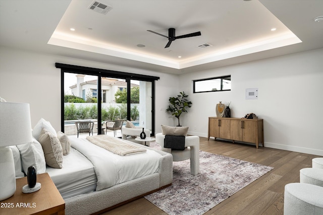 bedroom featuring access to exterior, a tray ceiling, visible vents, wood finished floors, and baseboards