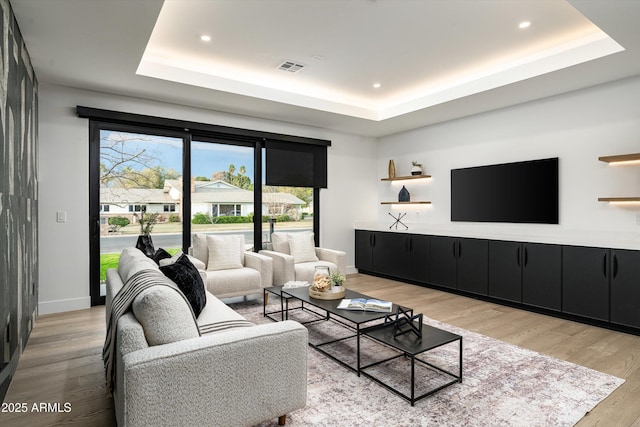 living room featuring a raised ceiling, baseboards, and light wood finished floors