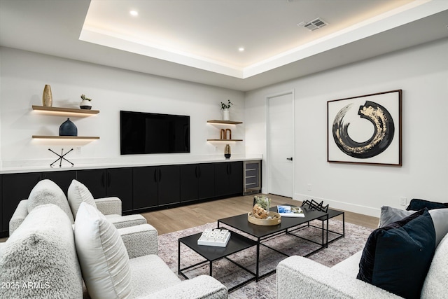 living room with light wood-style flooring, recessed lighting, beverage cooler, visible vents, and a tray ceiling