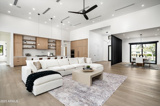 living area featuring light wood-style flooring, visible vents, a towering ceiling, and a ceiling fan