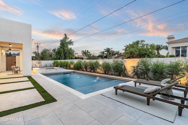 pool at dusk featuring a pool with connected hot tub, a fenced backyard, and a patio