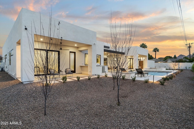 back of house at dusk with stucco siding, fence, a fenced in pool, and a patio