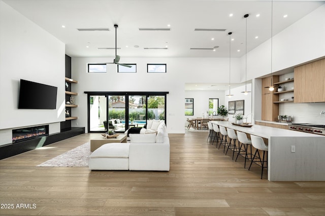 living area with light wood finished floors, a high ceiling, and a glass covered fireplace