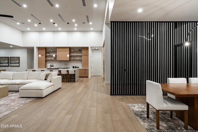 living room with light wood-style floors, a high ceiling, visible vents, and recessed lighting