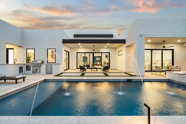 pool at dusk with area for grilling, a sink, a ceiling fan, and an outdoor pool