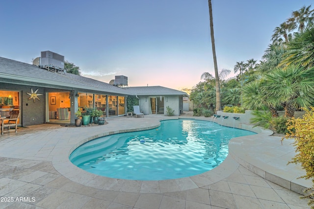 pool at dusk with pool water feature, a patio area, ceiling fan, and central air condition unit