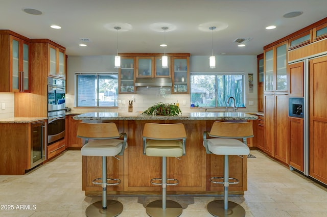 kitchen with wine cooler, decorative light fixtures, light stone countertops, and a kitchen island