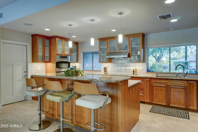 kitchen featuring a breakfast bar, pendant lighting, sink, stainless steel oven, and light stone counters