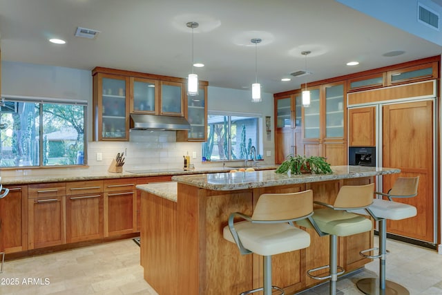 kitchen with light stone countertops, paneled fridge, a kitchen island, black electric cooktop, and decorative light fixtures