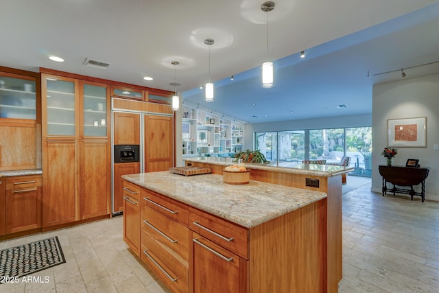 kitchen with a kitchen breakfast bar, hanging light fixtures, a center island, paneled built in fridge, and light stone counters