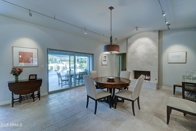 dining room with a tiled fireplace, track lighting, and lofted ceiling