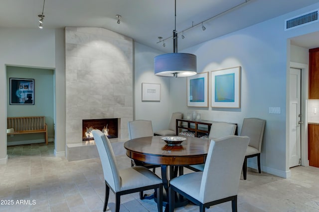 dining area featuring track lighting, vaulted ceiling, and a tile fireplace