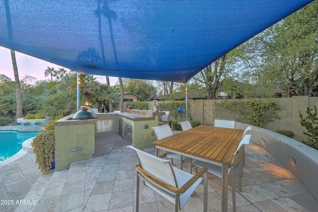 patio terrace at dusk with a fenced in pool, exterior kitchen, and a bar