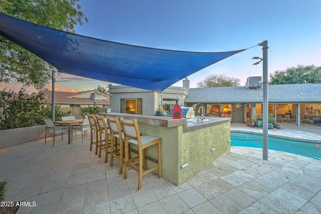 pool at dusk with a patio, a fireplace, and an outdoor bar