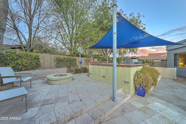 patio terrace at dusk featuring exterior kitchen and a fire pit