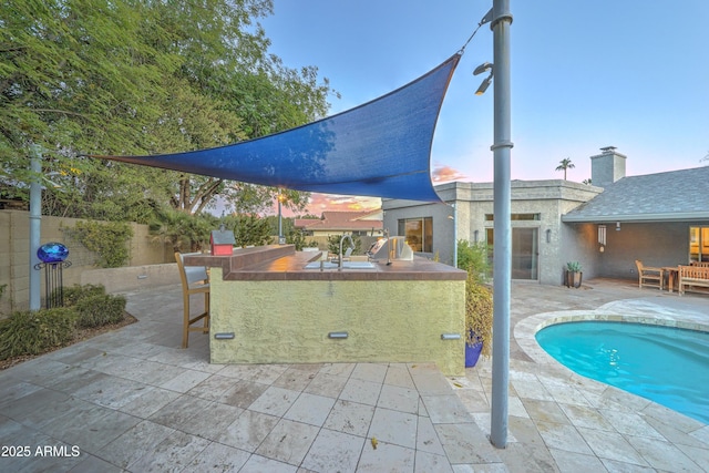 pool at dusk featuring area for grilling, an outdoor bar, and a patio area