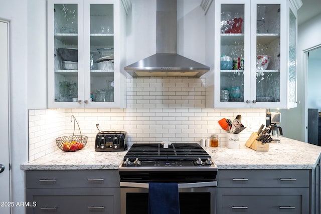 kitchen with wall chimney exhaust hood, gray cabinets, stainless steel range with gas cooktop, and glass insert cabinets