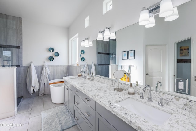 full bathroom with double vanity, wainscoting, tile patterned floors, a sink, and tile walls