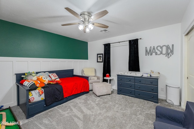 bedroom with a ceiling fan, wainscoting, visible vents, and light colored carpet