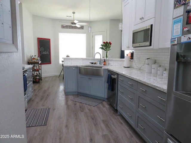 kitchen featuring stainless steel appliances, decorative backsplash, white cabinetry, a sink, and wood finished floors