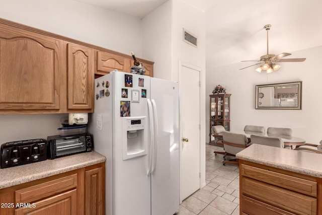 kitchen featuring white refrigerator with ice dispenser, a ceiling fan, light tile patterned floors, and light countertops