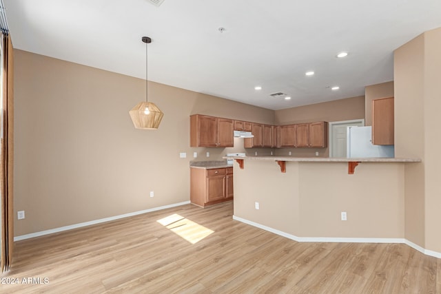 kitchen with kitchen peninsula, a breakfast bar area, light wood-type flooring, pendant lighting, and white refrigerator