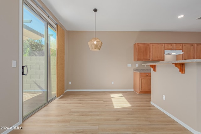 kitchen featuring a kitchen bar, hanging light fixtures, light hardwood / wood-style floors, and kitchen peninsula