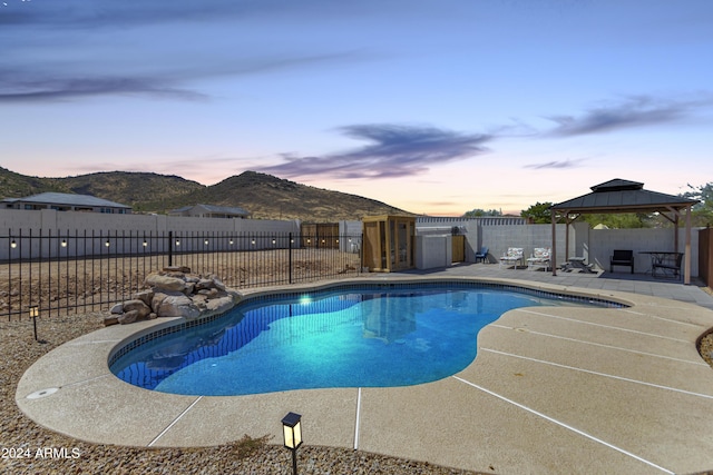 pool at dusk with a gazebo, a mountain view, and a patio area